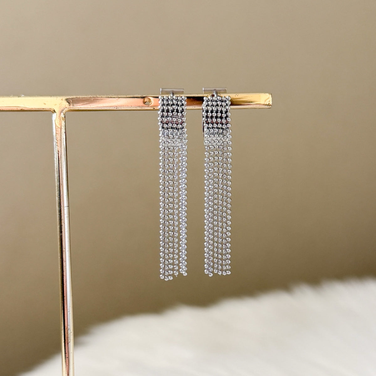 Silver chain earrings on a gold stand against a beige background