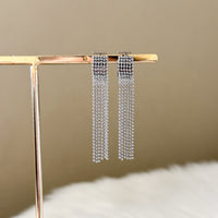 Silver chain earrings on a gold stand against a beige background